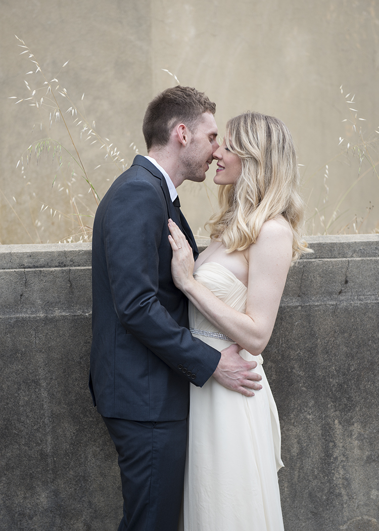 Bride and groom kissing next to concrete