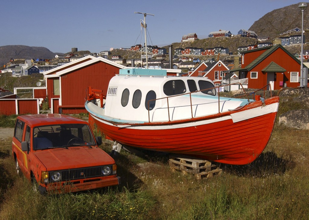 Red and white boat on blocks next to red car in Qaqortoq, Greenland