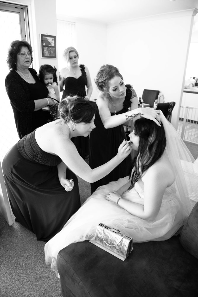 Black and white photo of everyone looking at bride. Getting last minute veil and make up put on. Bride getting ready.