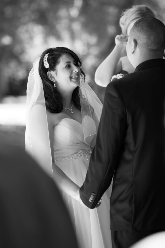 Black and white photo of bride during ceremony. Funny moment. Smiling. Holding hands with the groom