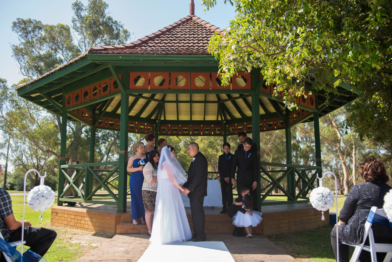 Bride and groom holding hands during their ceremony. Wide shot showing all the bridal party. Their son and daughter hugging