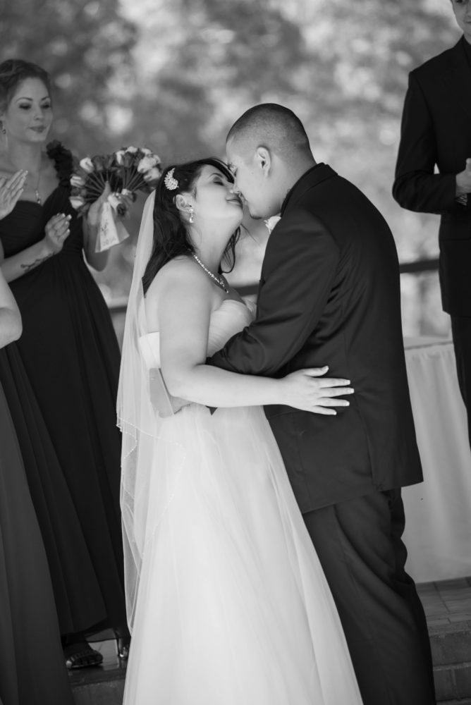 Black and white photo of bride and groom almost kissing during wedding ceremony. Smiling and eyes closed