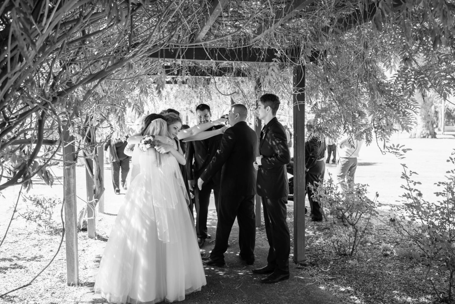 Black and white photo of sister hugging bride after the wedding ceremony. Under canopy of wisteria. At Stirling Square, Guildford.