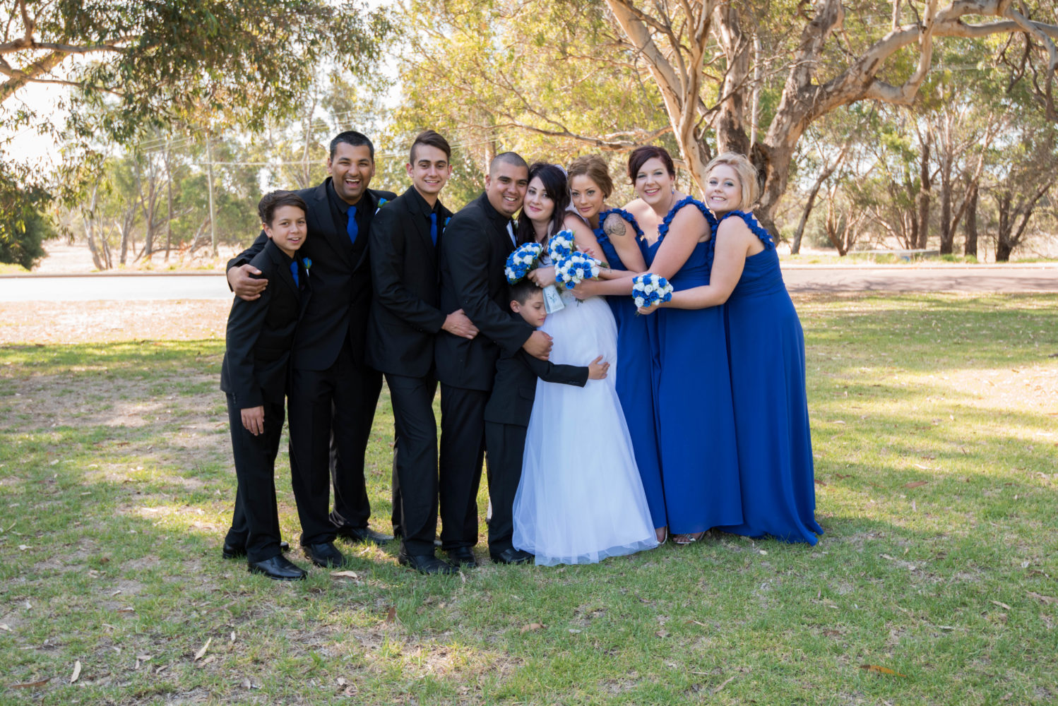 Colour photo of group shot of bridal party. Group hug. Son hugging his mum