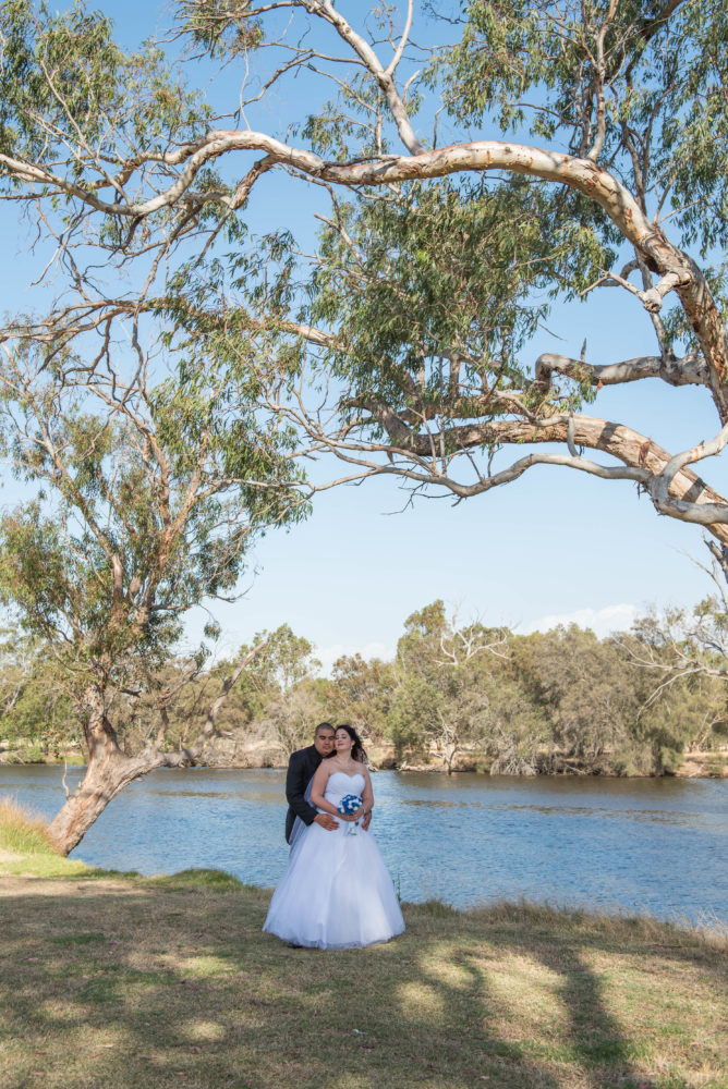 Bride and groom standing on the banks of the Swan river, Perth. Surrounded by native trees.