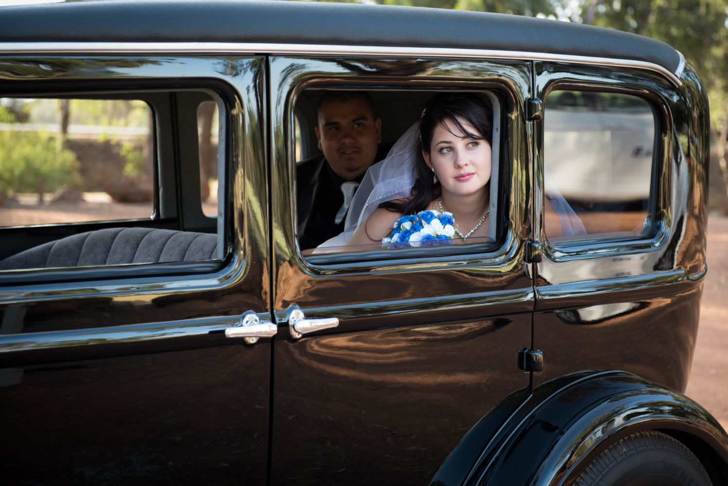 Bride looking out of her bridal car, looking up at the sky. Looking wistful. Groom looking at her from inside. Black wedding car