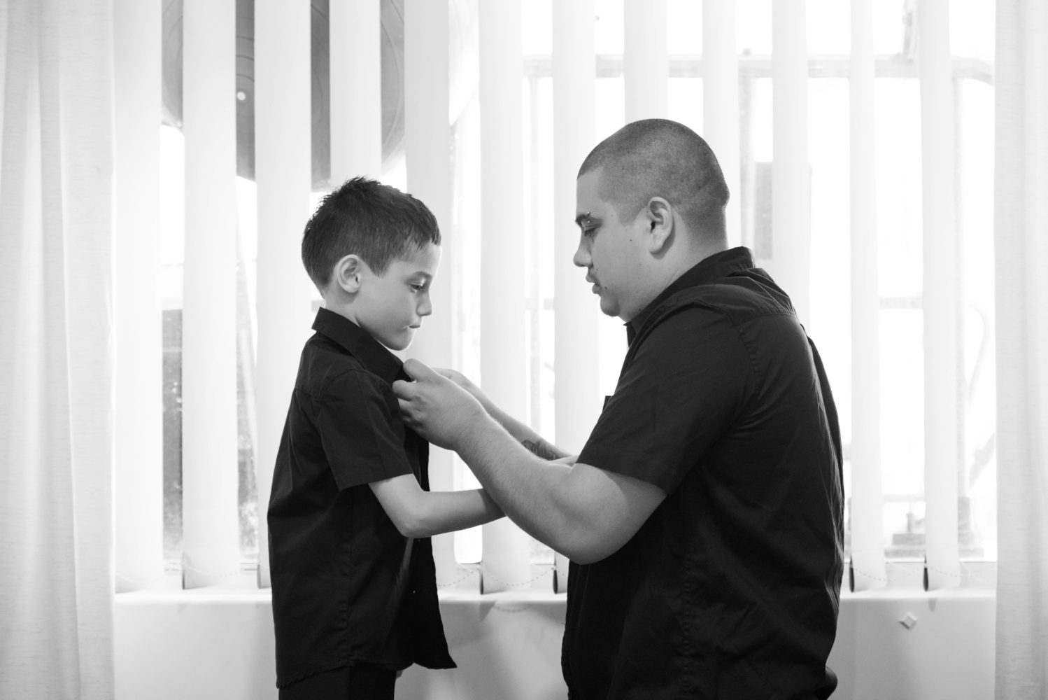 Dad and son getting ready for wedding. Doing up their shirt button. Black and white wedding photo