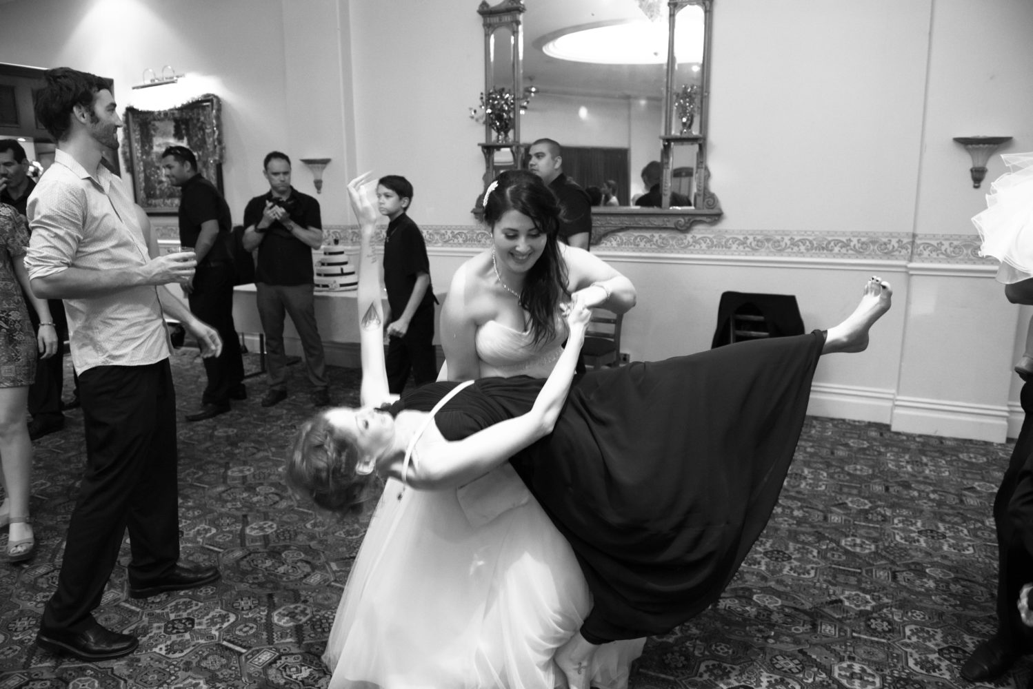 Black and white photo of sisters dancing during wedding reception. Bride is dipping her sister. Funny moment during wedding