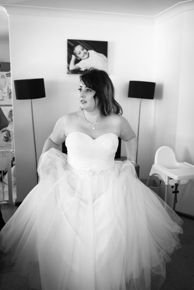 Black and white photo of bride getting ready. Lifting wedding dress