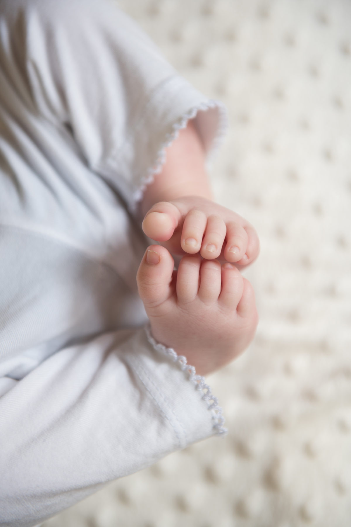 Close up of baby's toes touching on a cream blanket