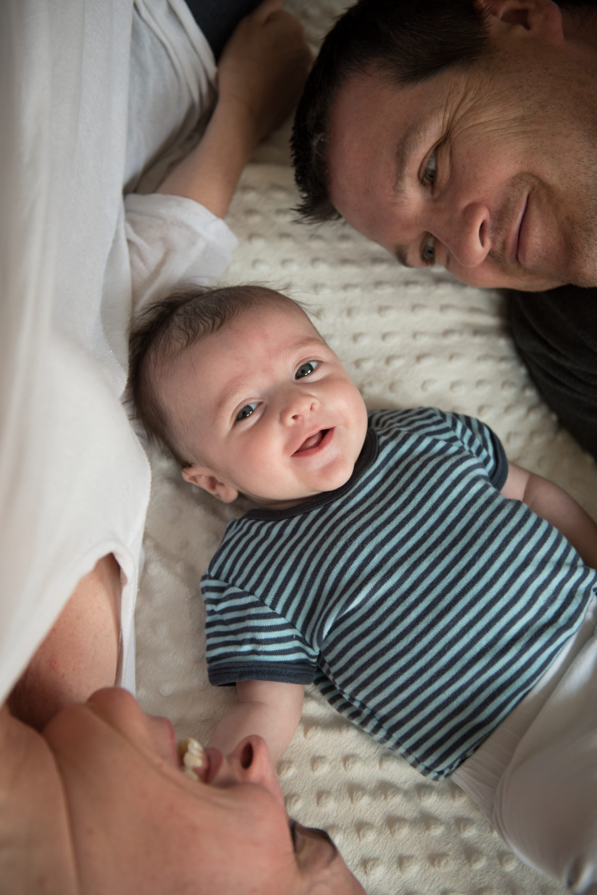 Mother and father laying around their baby looking at the camera