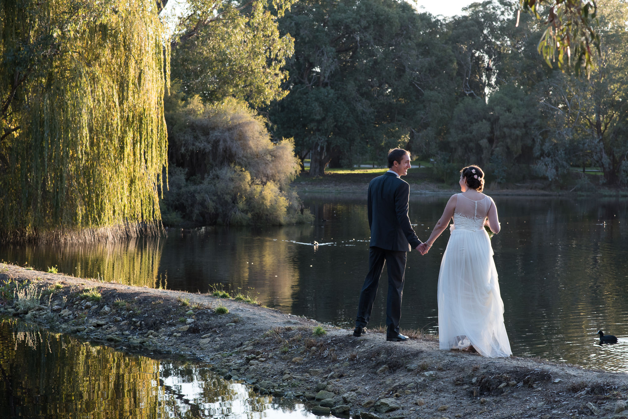 bride and groom walk along lake in afternoon light with weeping willows