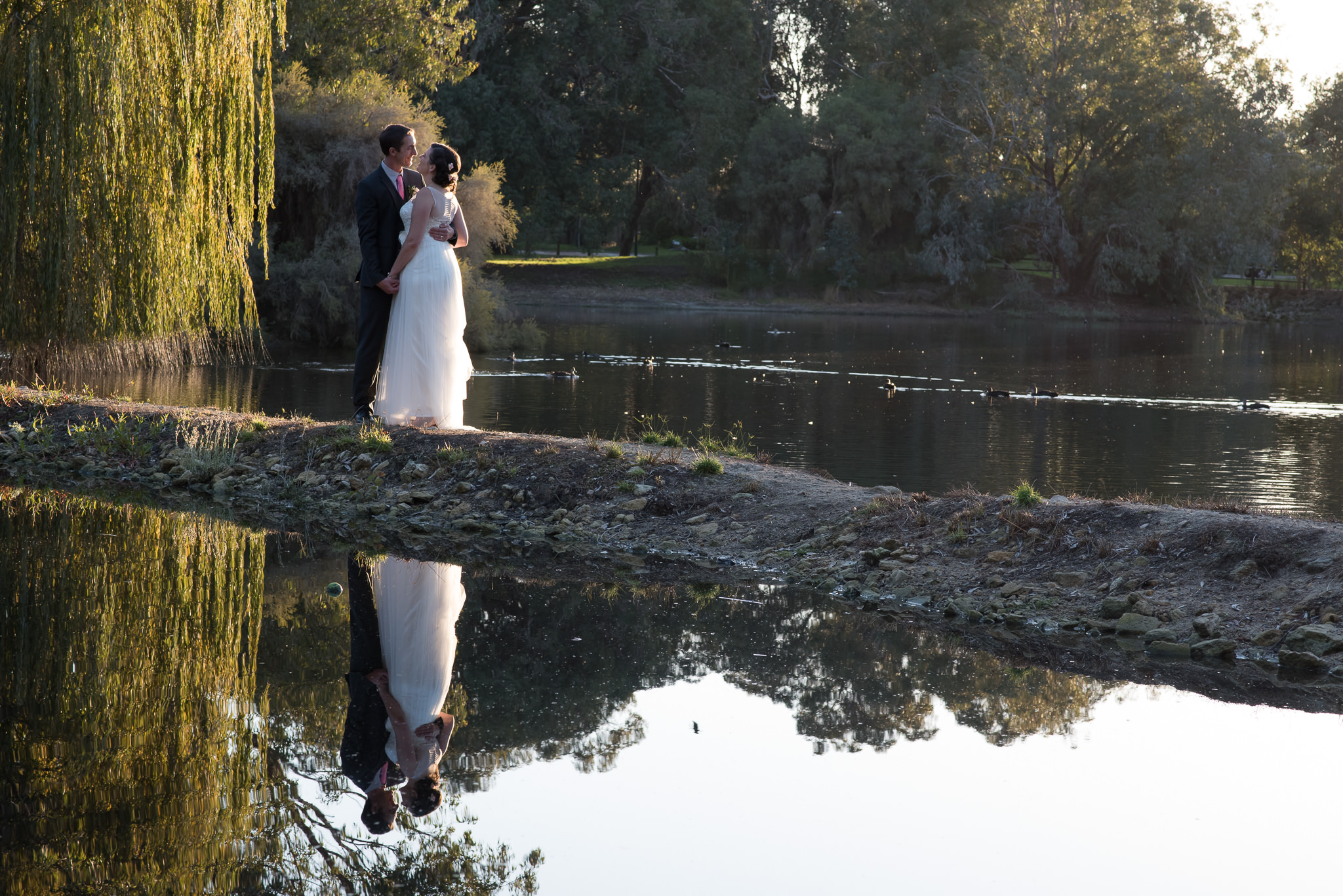 bride and groom hold each other with lake reflection