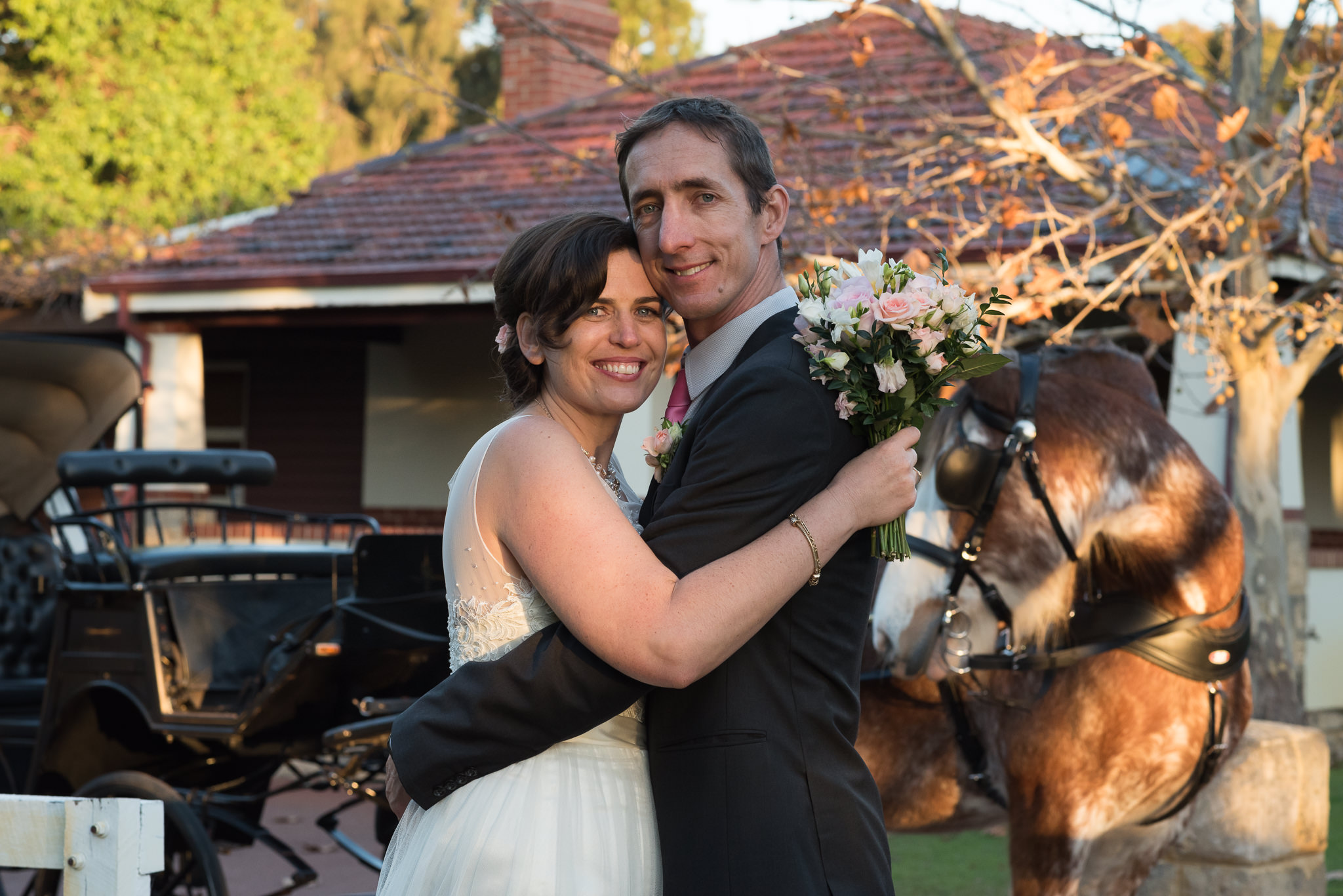 bride and groom look at camera in front of their horse and carriage