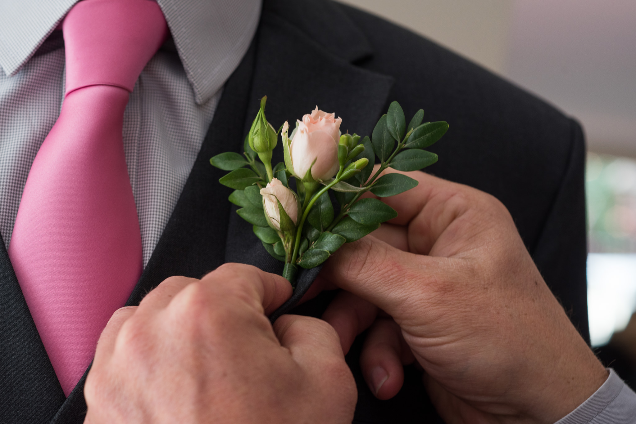 hands placing a small pink rose buttonhole on a jacket