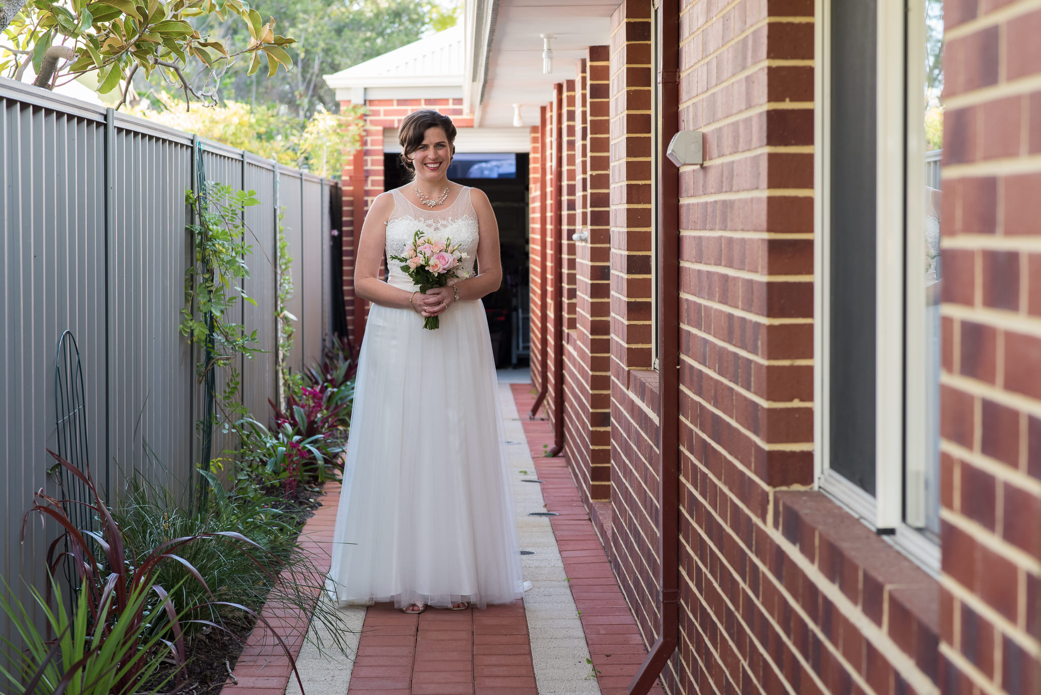 bride waits at the side of the house to go to her backyard ceremony