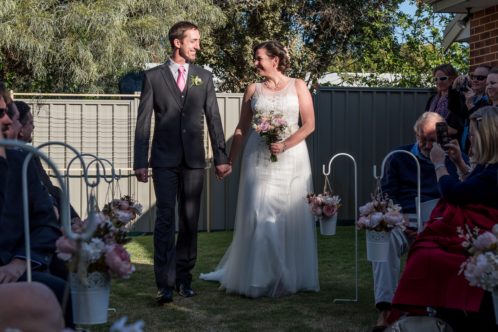 bride and groom smile together and walk down their backyard wedding aisle