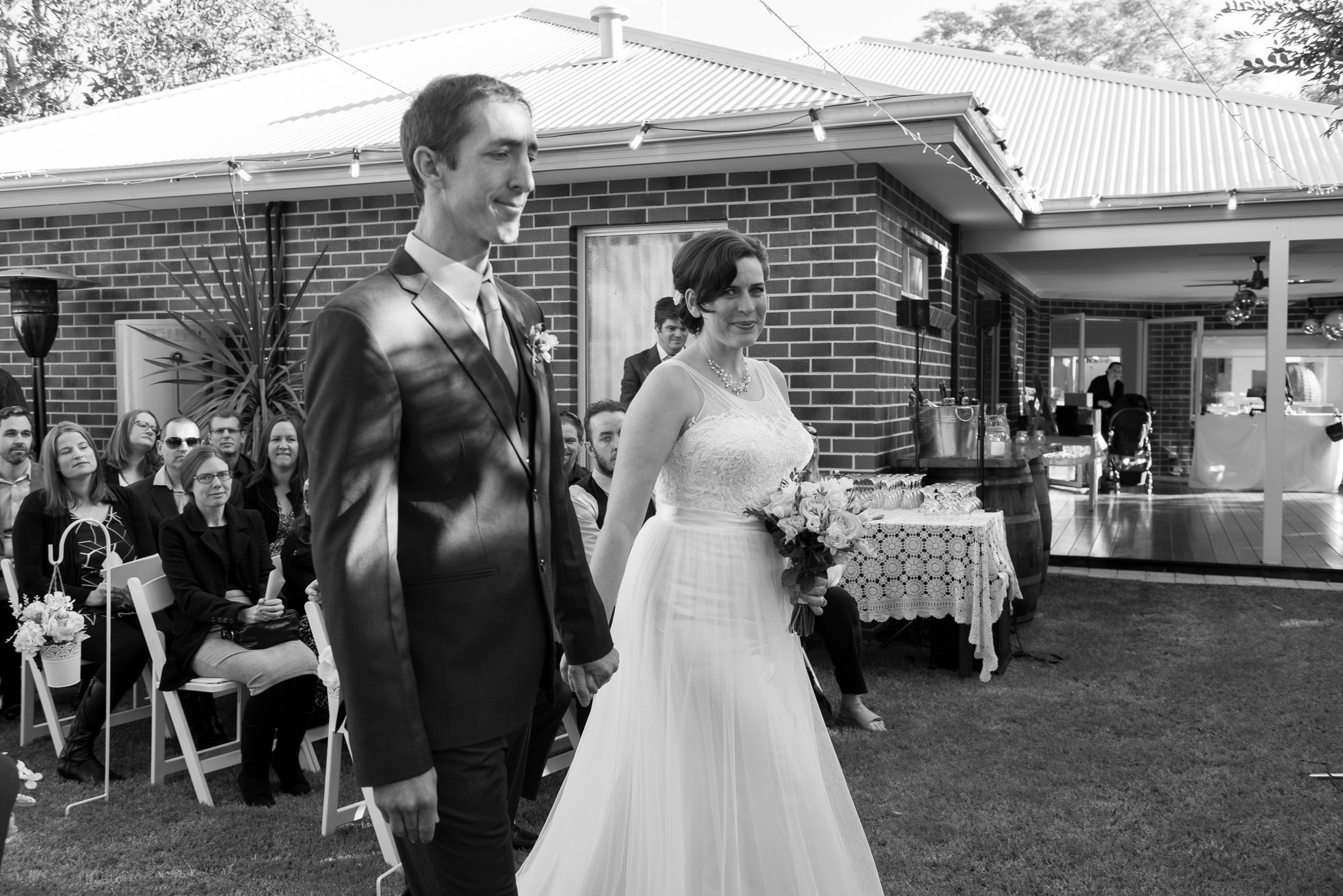 bride and groom walk down the aisle together in backyard