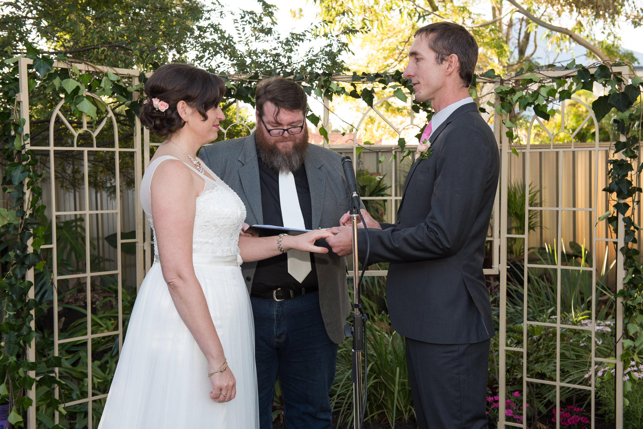 groom places ring on bride's finger in backyard wedding