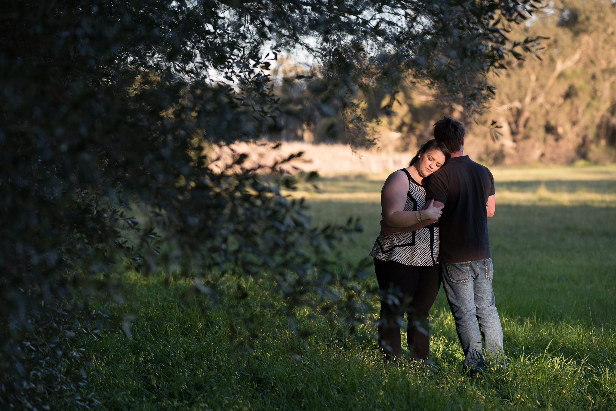 girl rests her head on her fiancee's shoulder at Yellagonga park, her eyes closed