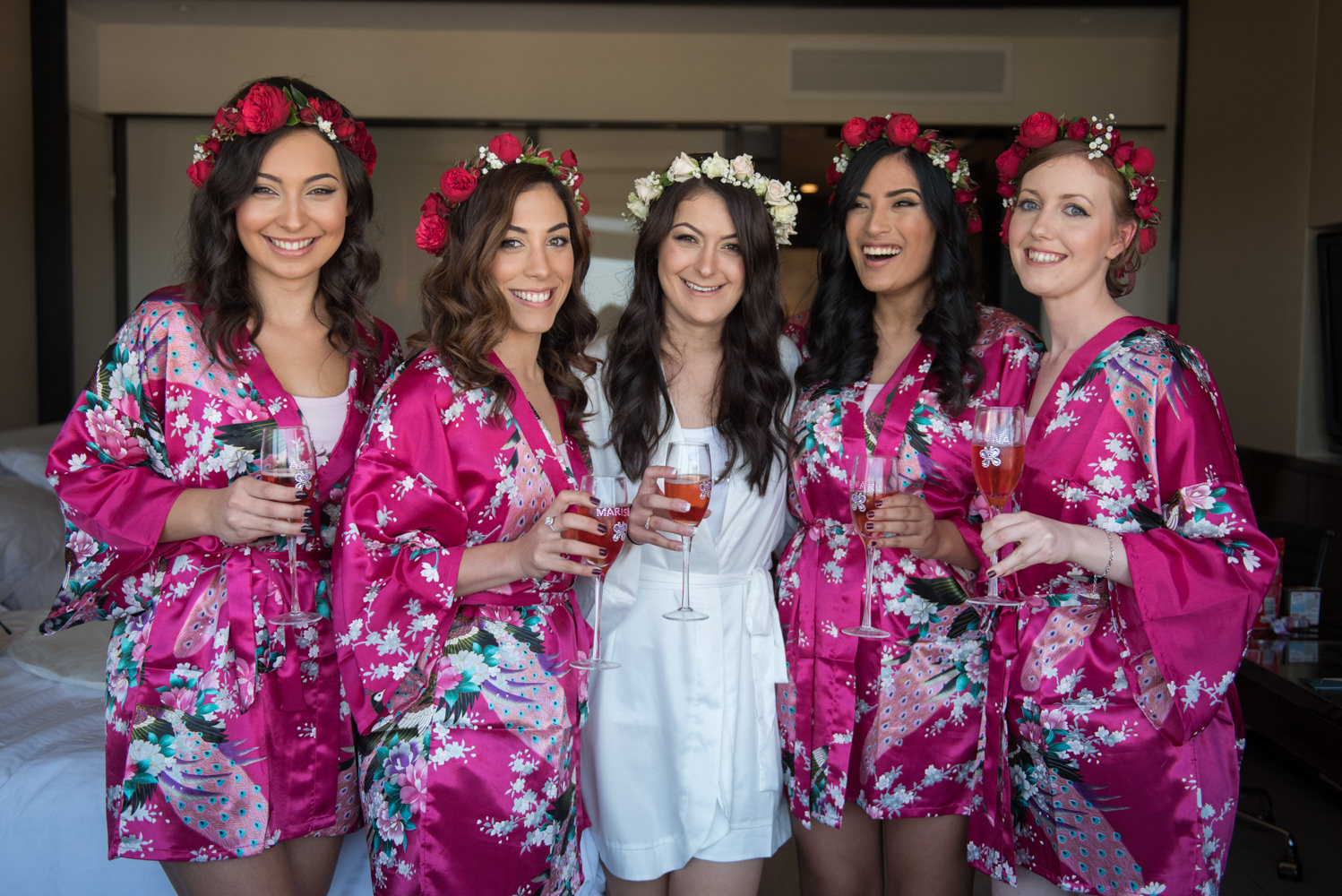 Bride and bridesmaids hugging and drinking champagne in silk gowns