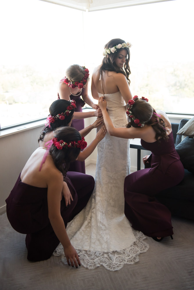 Bridesmaids helping bride into her dress, doing up the buttons, elegant