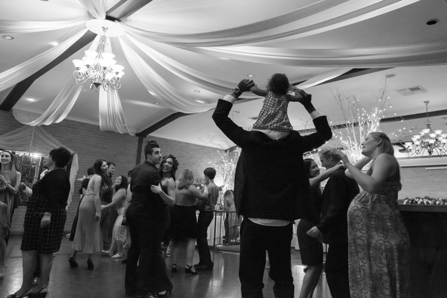 Child sitting on father's shoulders on the wedding dance floor