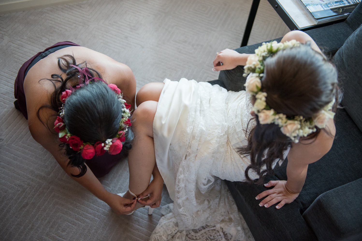 Bridesmaid helping bride do up her show from above, flower crowns