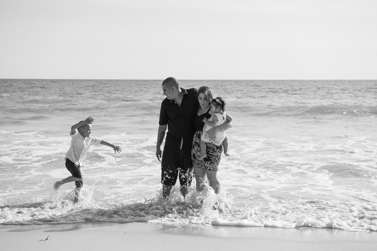 little boy splashing in the ocean around his family