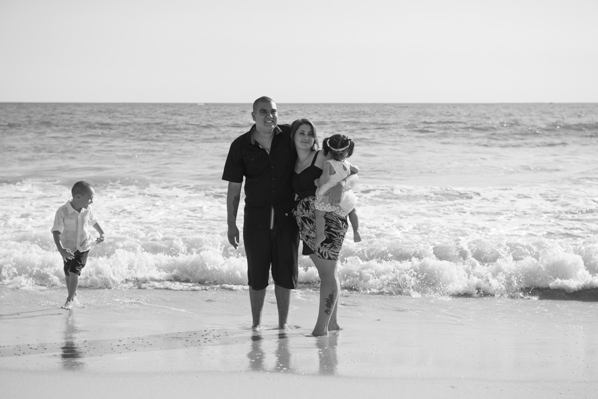 family portrait standing in the ocean with little boy running around