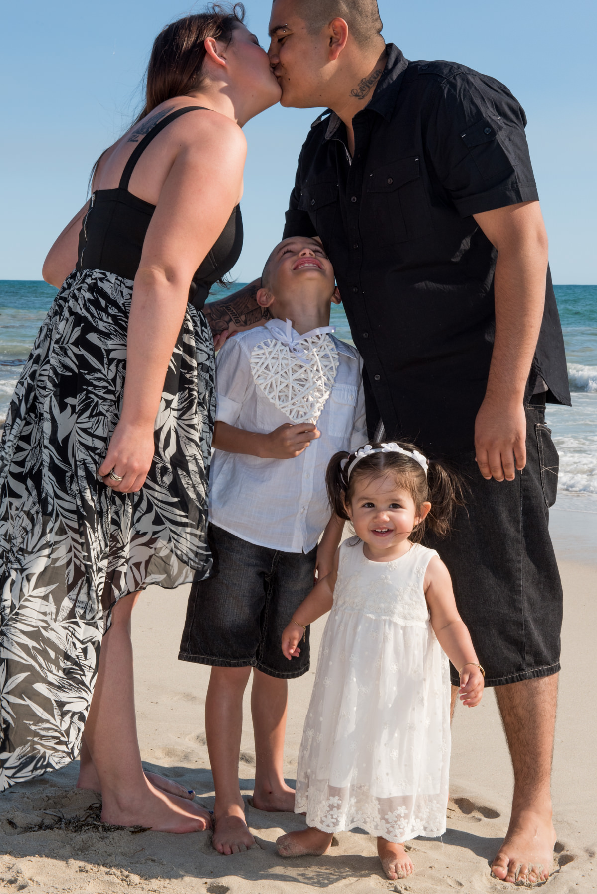 little kids smiling beneath their parents kissing on the beach