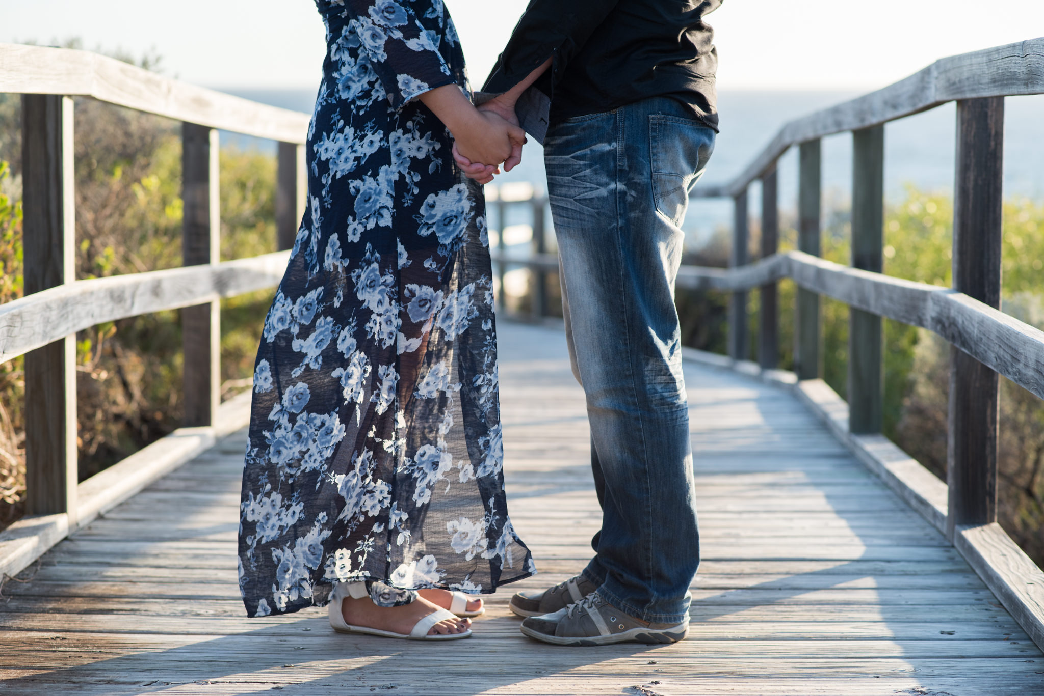 Close up of the lower half of boy and girl holding hands at the beach, legs and feet