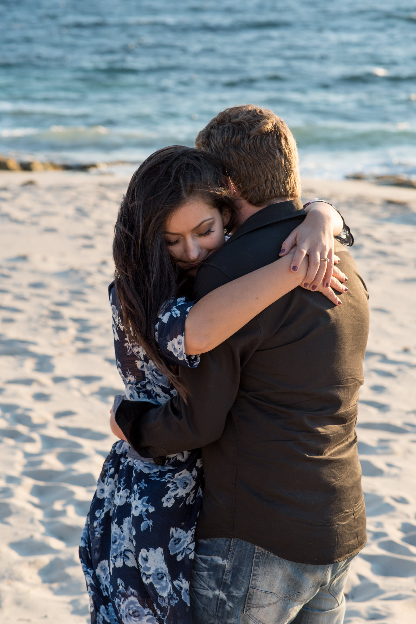 Girl hugging boy at beach and smiling with eyes closed