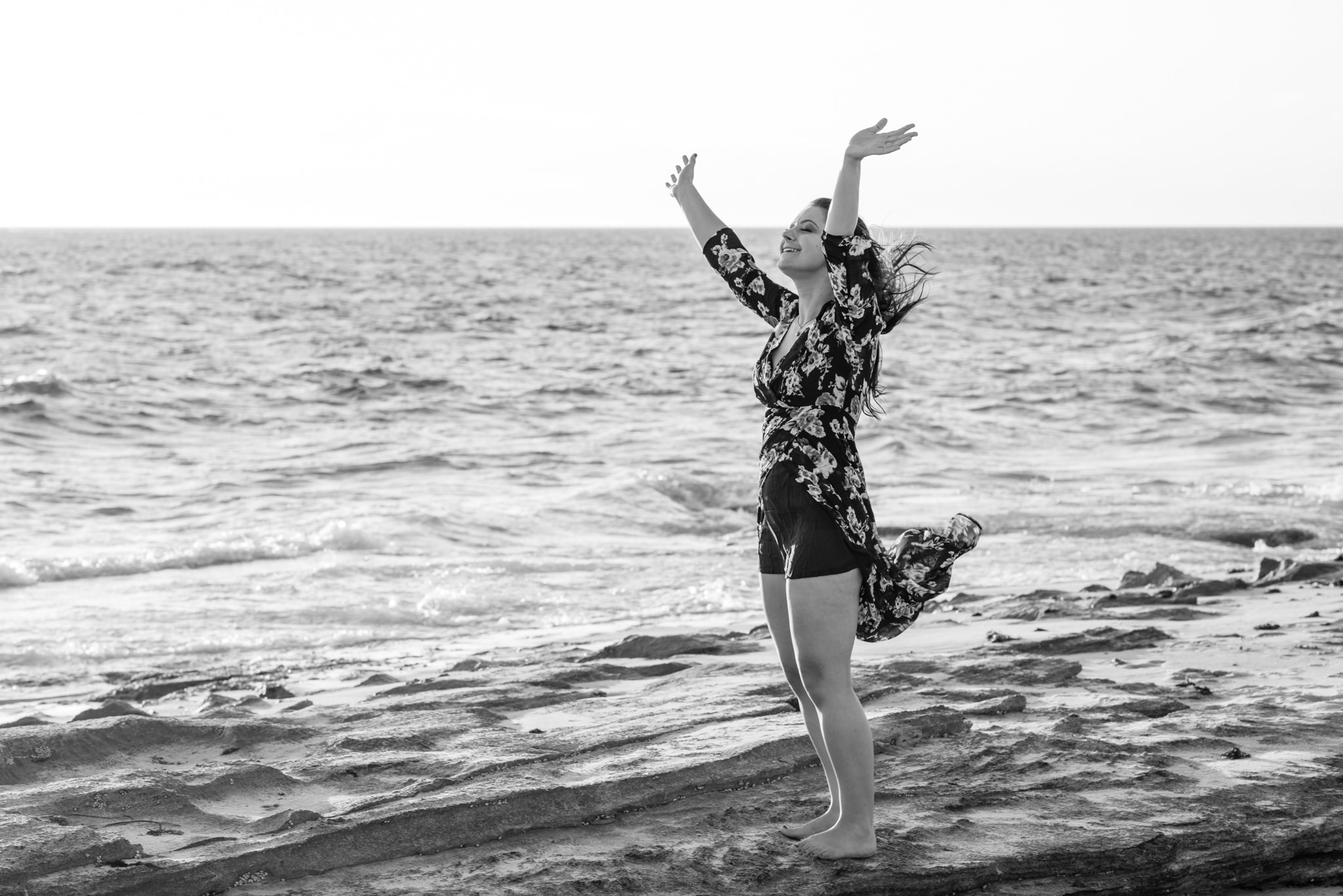 Girl on the rocks at the beach throwing her hands in the air