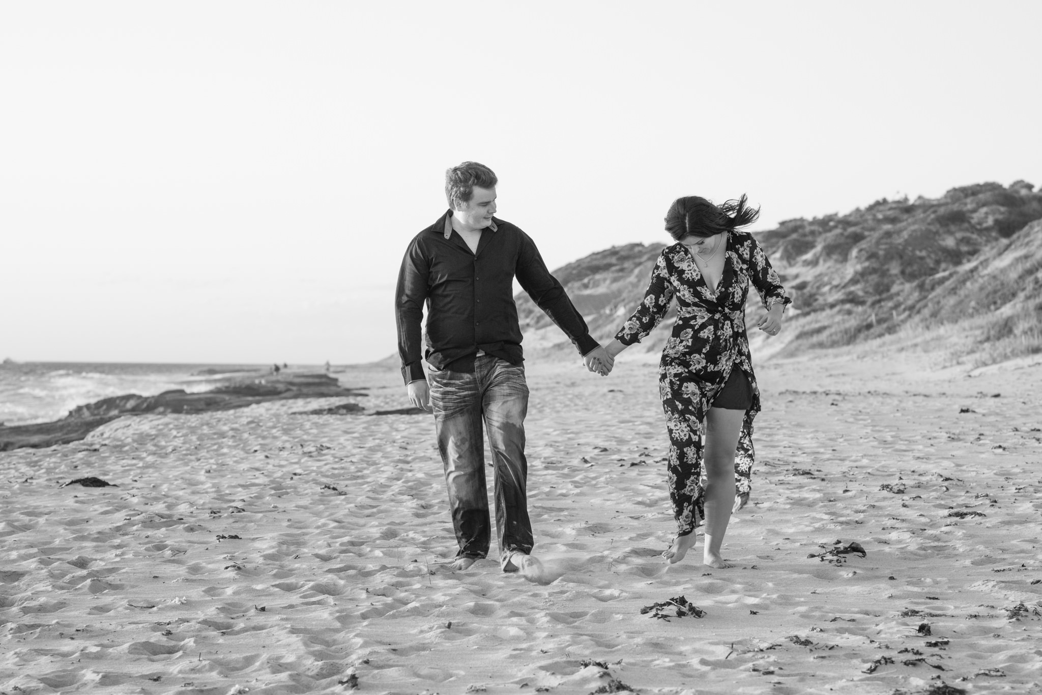 Black and white photo of girl and boy holding hands walking on Burns beach