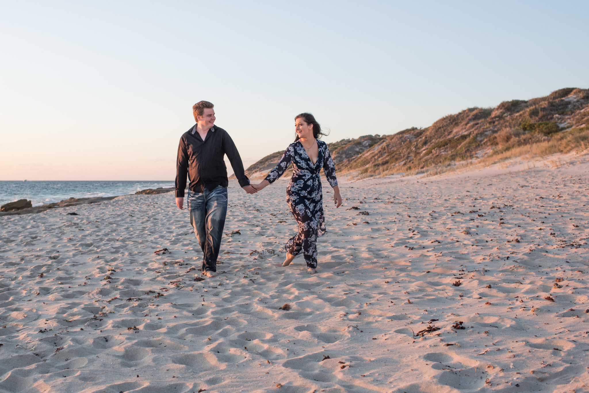 guy and girl holding hands walking on Burns beach looking at each other