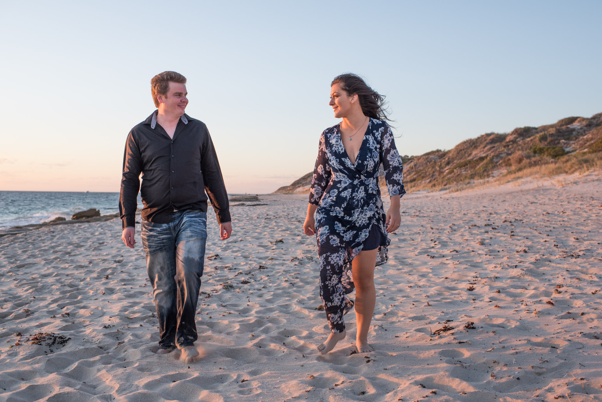 guy and girl walk along beach looking at each other