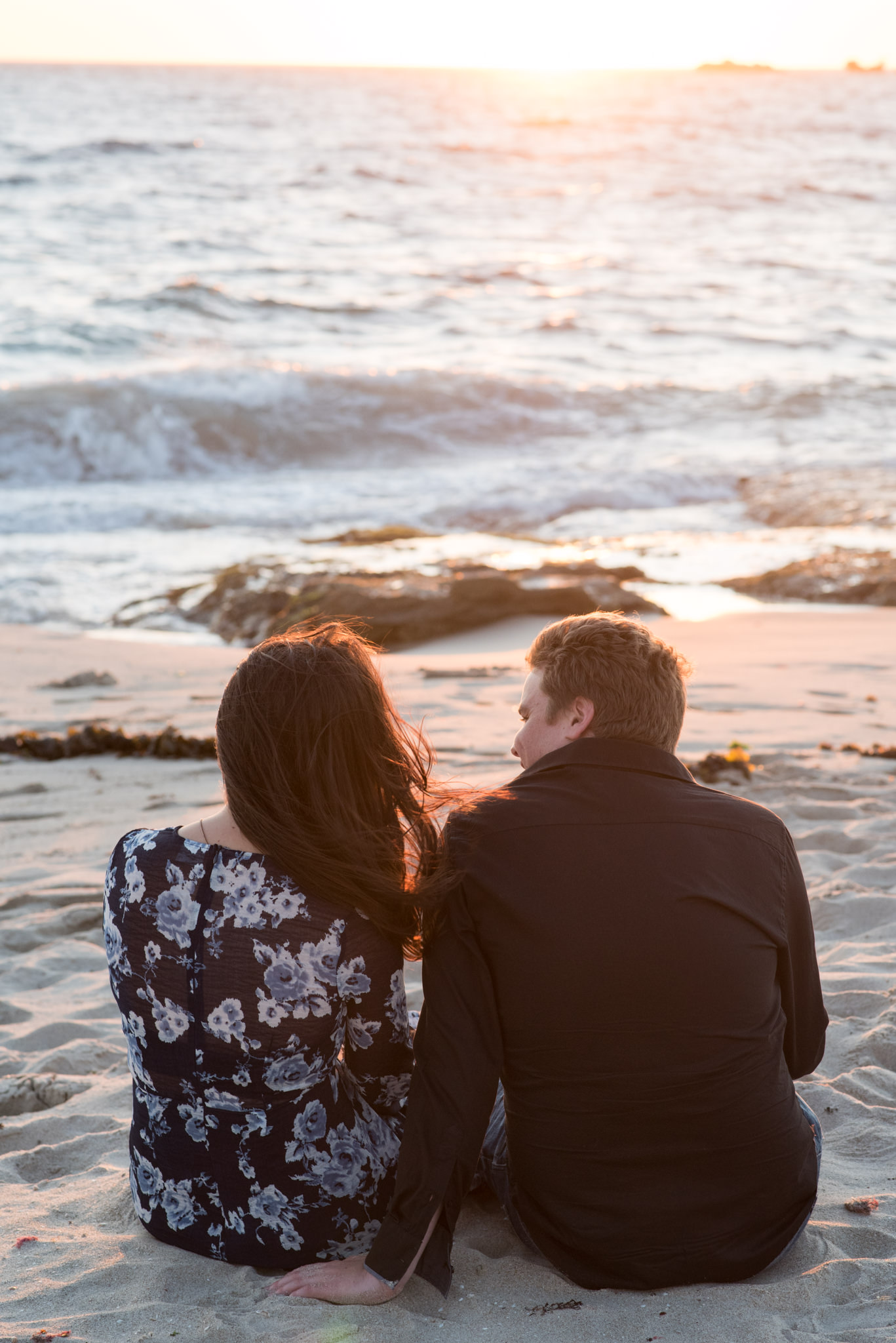 Guy looks at girl sitting on the beach at sunset