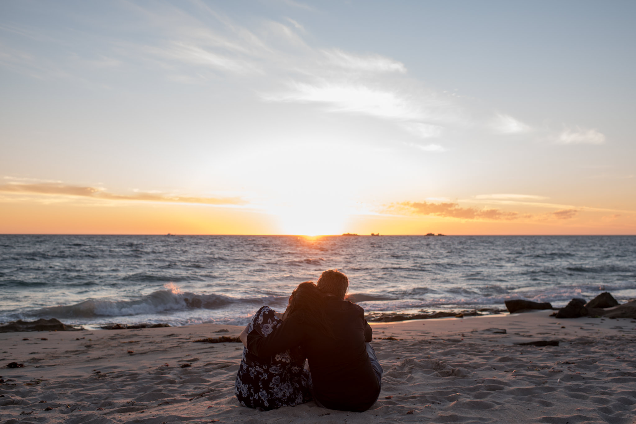 Couple sitting on Burns beach watching the sun set, heads together