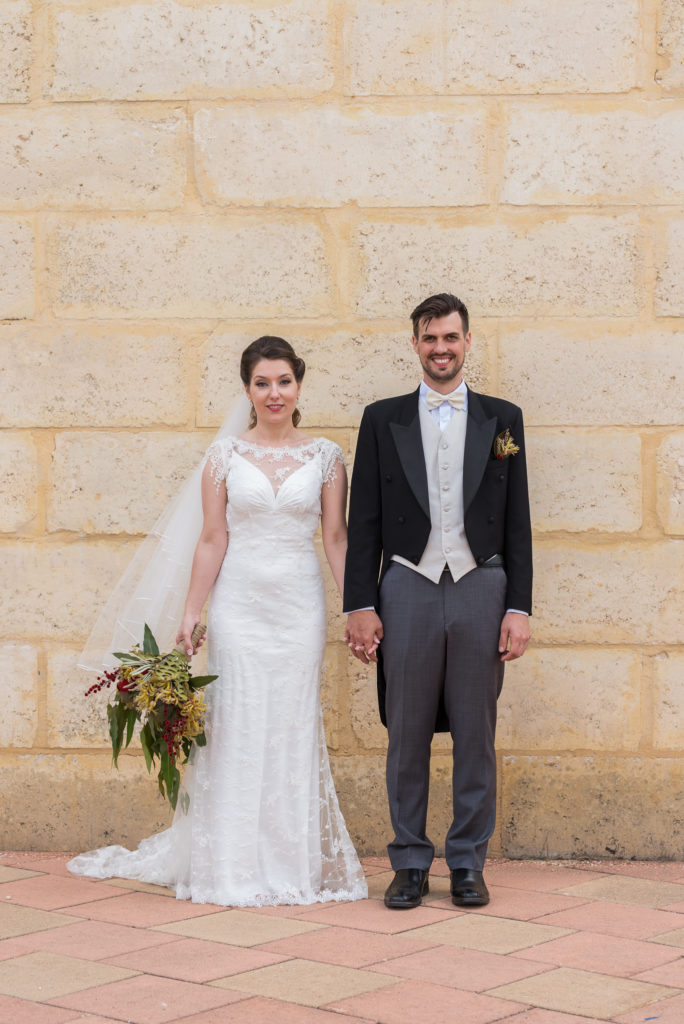 Bride and groom stand against yellow brick wall