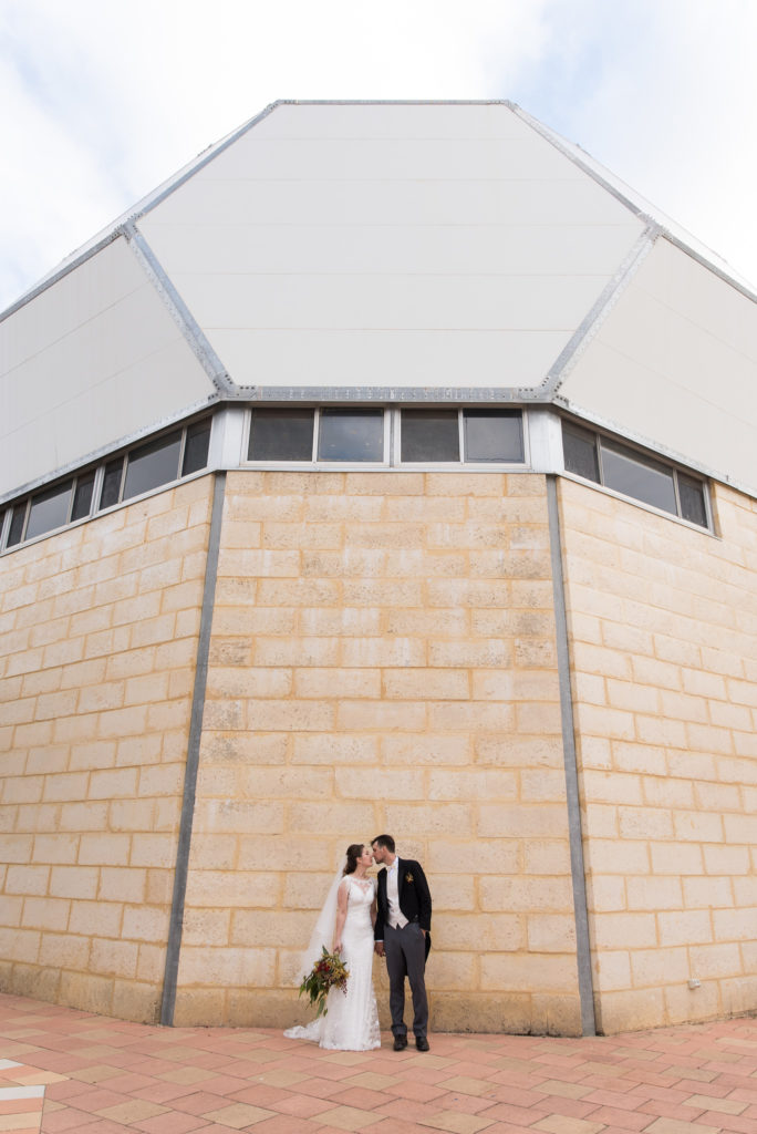 Bride and groom kiss against the wall of the Cosmology Gallery