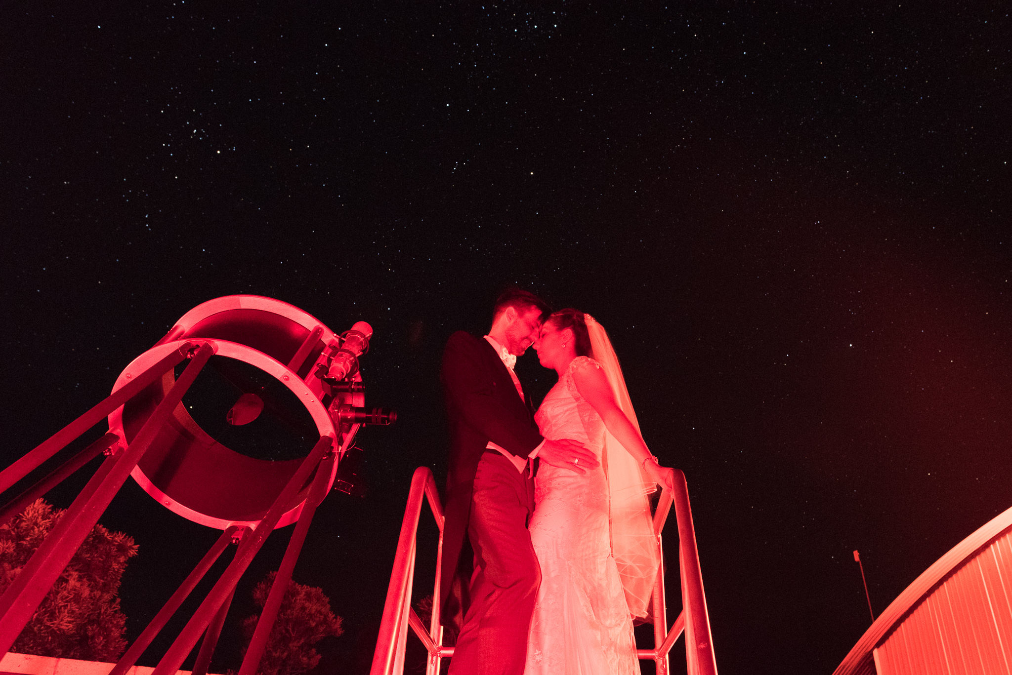 Wedding couple standing near telescope under the stars