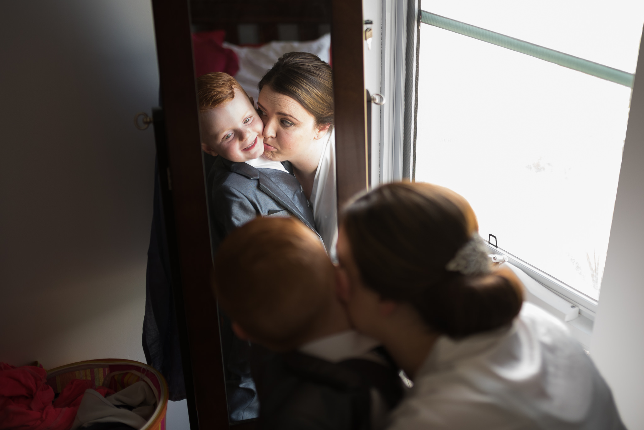 bride cuddles page boy as he gets dressed in front of mirror