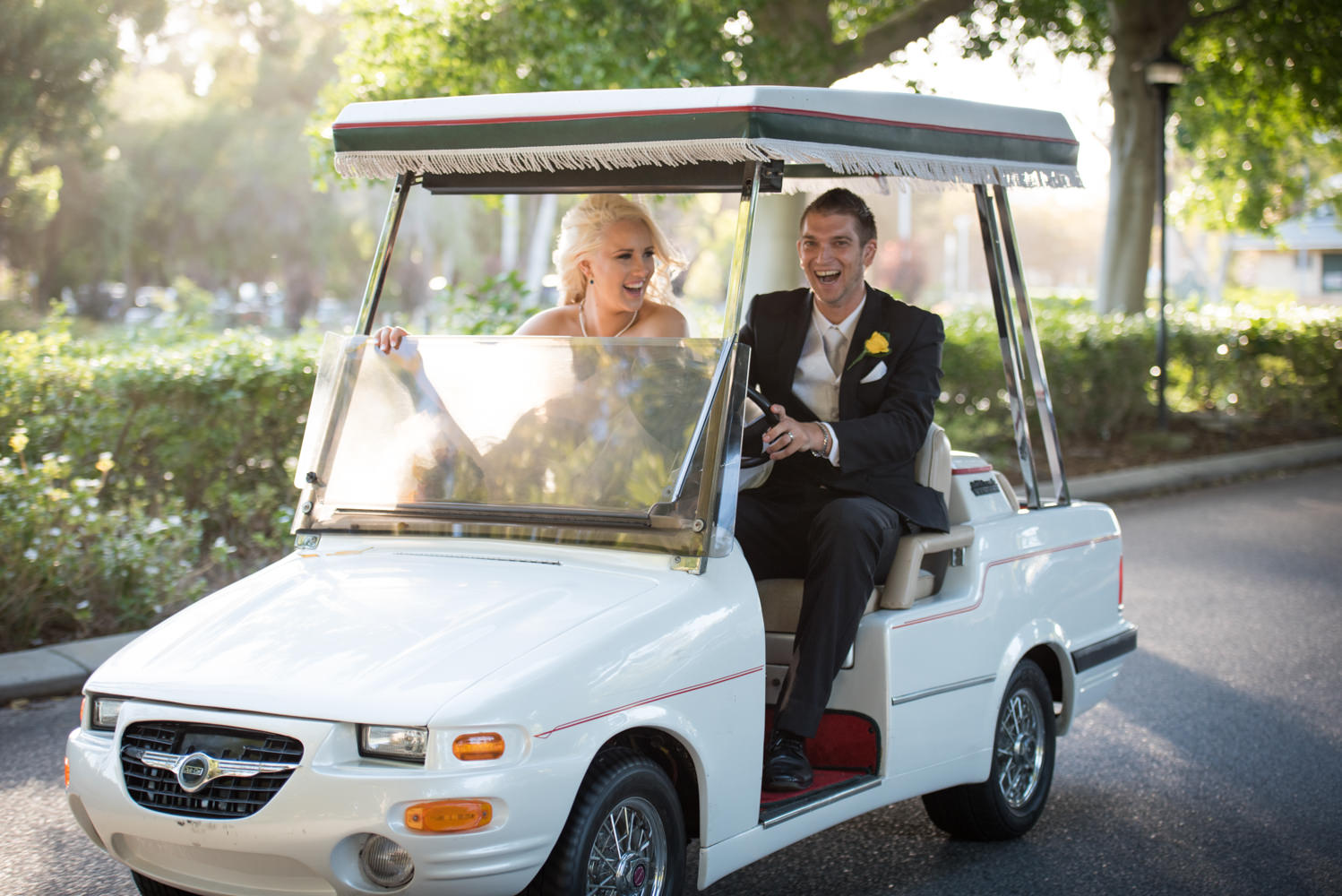 Bride and groom driving golf cart to reception laughing