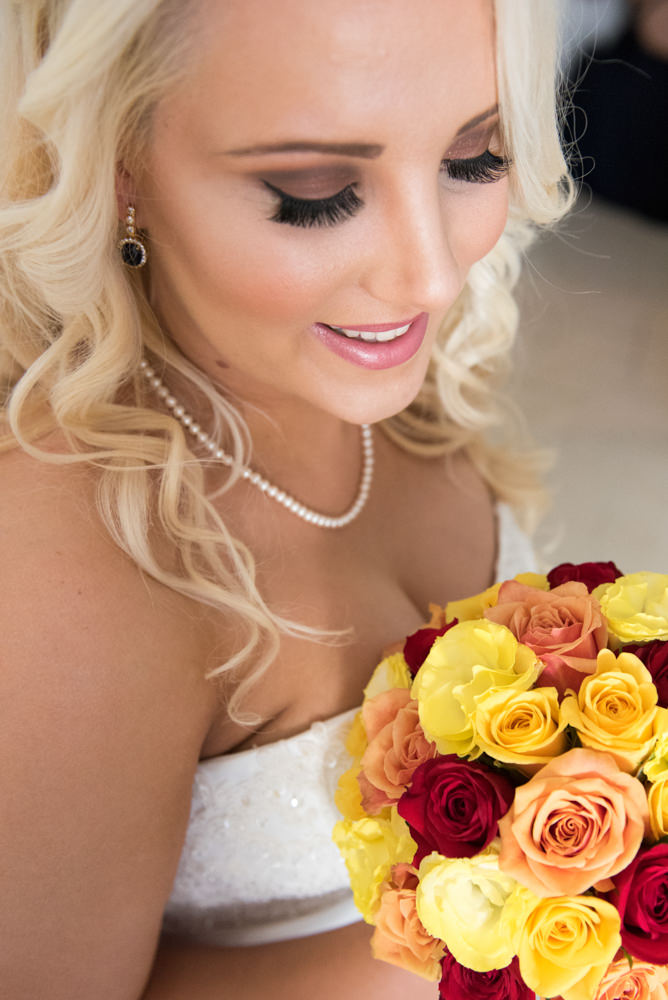 Close up of bride looking down at her bouquet of yellow and red roses