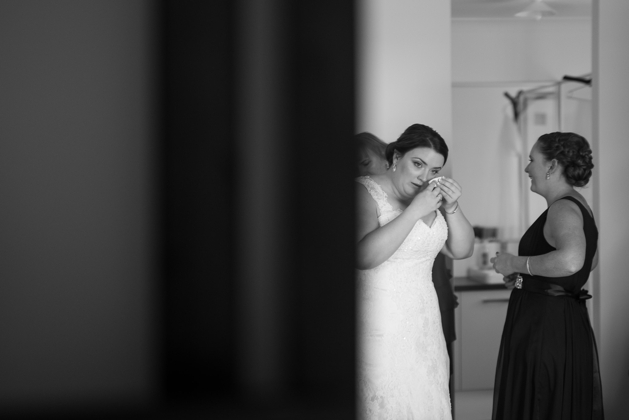 bride dabs tear away while getting her wedding dress on