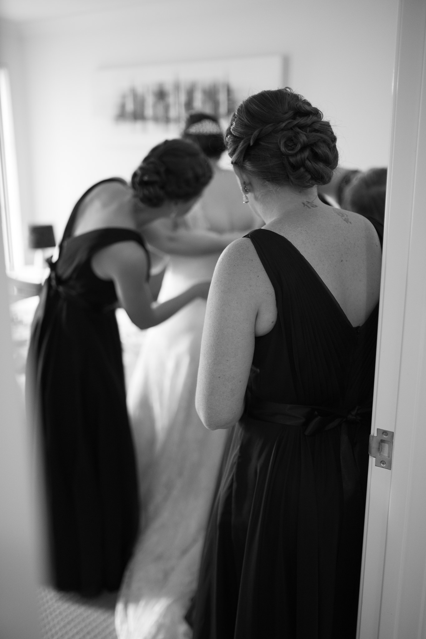 bridesmaid looks on while bride has her dress done up