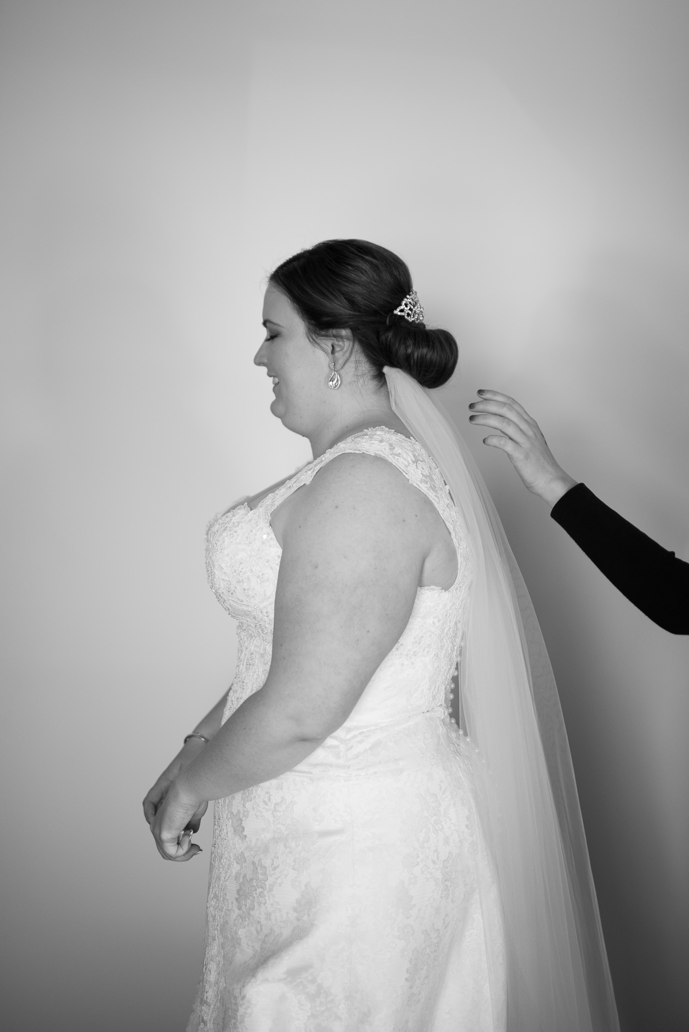 hair stylist reaches to adjust the bride's veil