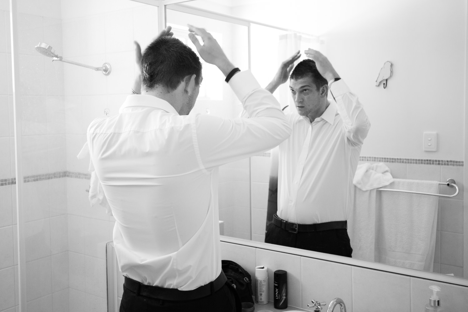 Groom in bathroom doing his hair infront of mirror