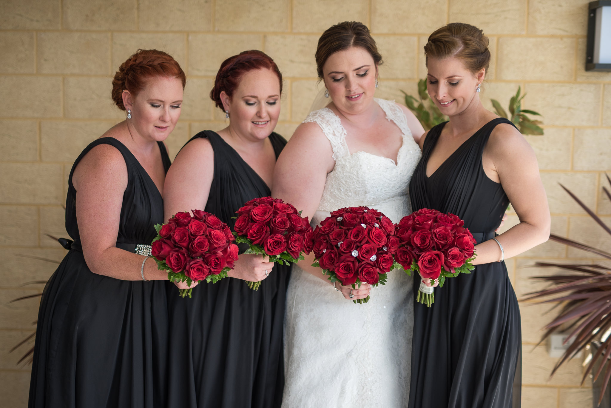 bride and her bridesmaids looking down at their red rose bouquets